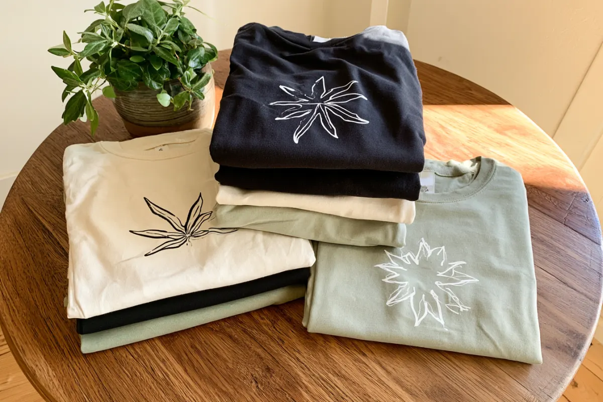 Folded custom tees with line art designs in cream, black and sage