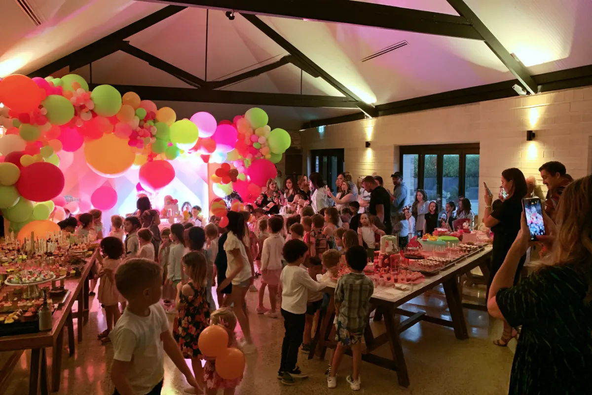 Kids and parents crowding a bright balloon backdrop at a birthday party