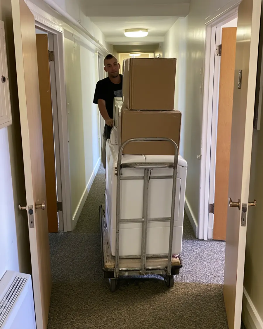 A mover pushing a loaded hand truck down an apartment hallway