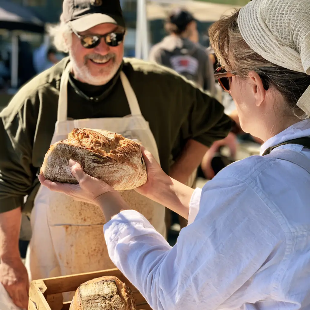 A customer taking a whole wheat loaf from the baker across the table